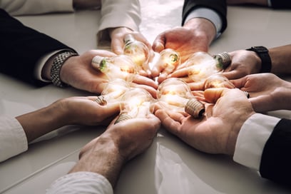 This image showcases "shared vision" with multiple hands in a circle each with an illuminated light bulb. 